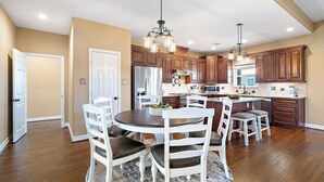 A spacious kitchen with wooden cabinets, a central island, and a dining area with white chairs. - Copper Top by Ryson Vacation Rentals (Galveston)