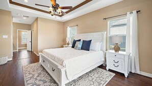 A bedroom with a large bed, a nightstand, a ceiling fan, and a window with curtains. - Copper Top by Ryson Vacation Rentals (Galveston)