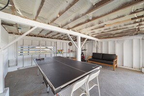 A ping pong table in a room with a high ceiling, white walls, and a wooden bench. - Colva Tides by Ryson Vacation Rentals (Galveston)