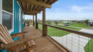 A wooden deck with a view of a residential area, including houses and a road. - Coral Mountain by Ryson Vacation Rentals (Galveston)