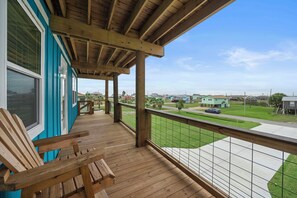 A wooden deck with a view of a residential area, including houses and a road. - Coral Mountain by Ryson Vacation Rentals (Galveston)