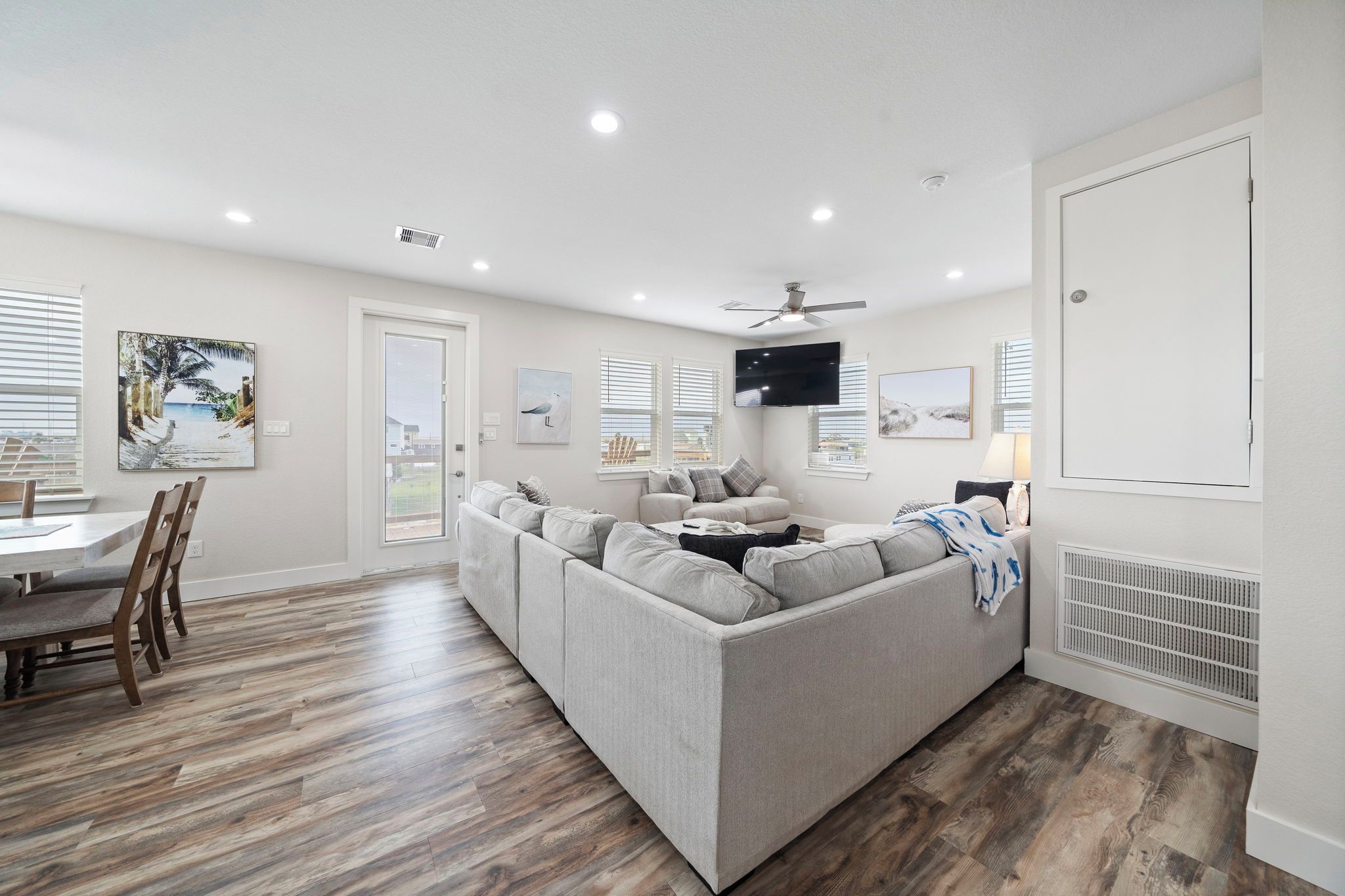 Uma sala de estar moderna com um sofá modular cinza, piso de madeira e um ventilador de teto.