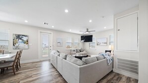 A modern living room with a gray sectional sofa, wooden flooring, and a ceiling fan. - Coral Mountain by Ryson Vacation Rentals (Galveston)