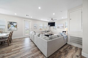 A modern living room with a gray sectional sofa, wooden flooring, and a ceiling fan. - Coral Mountain by Ryson Vacation Rentals (Galveston)