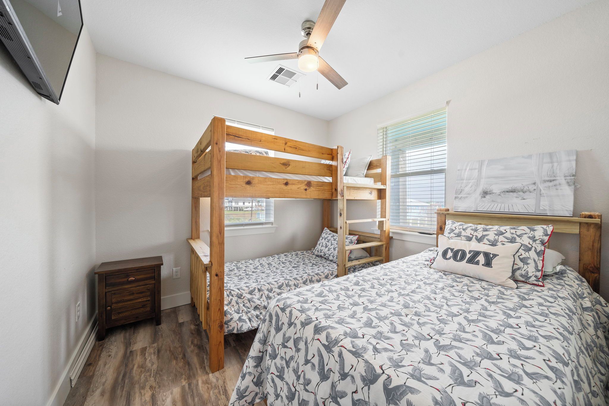 A bedroom with bunk beds, a ceiling fan, a small bedside table, and a window with blinds.