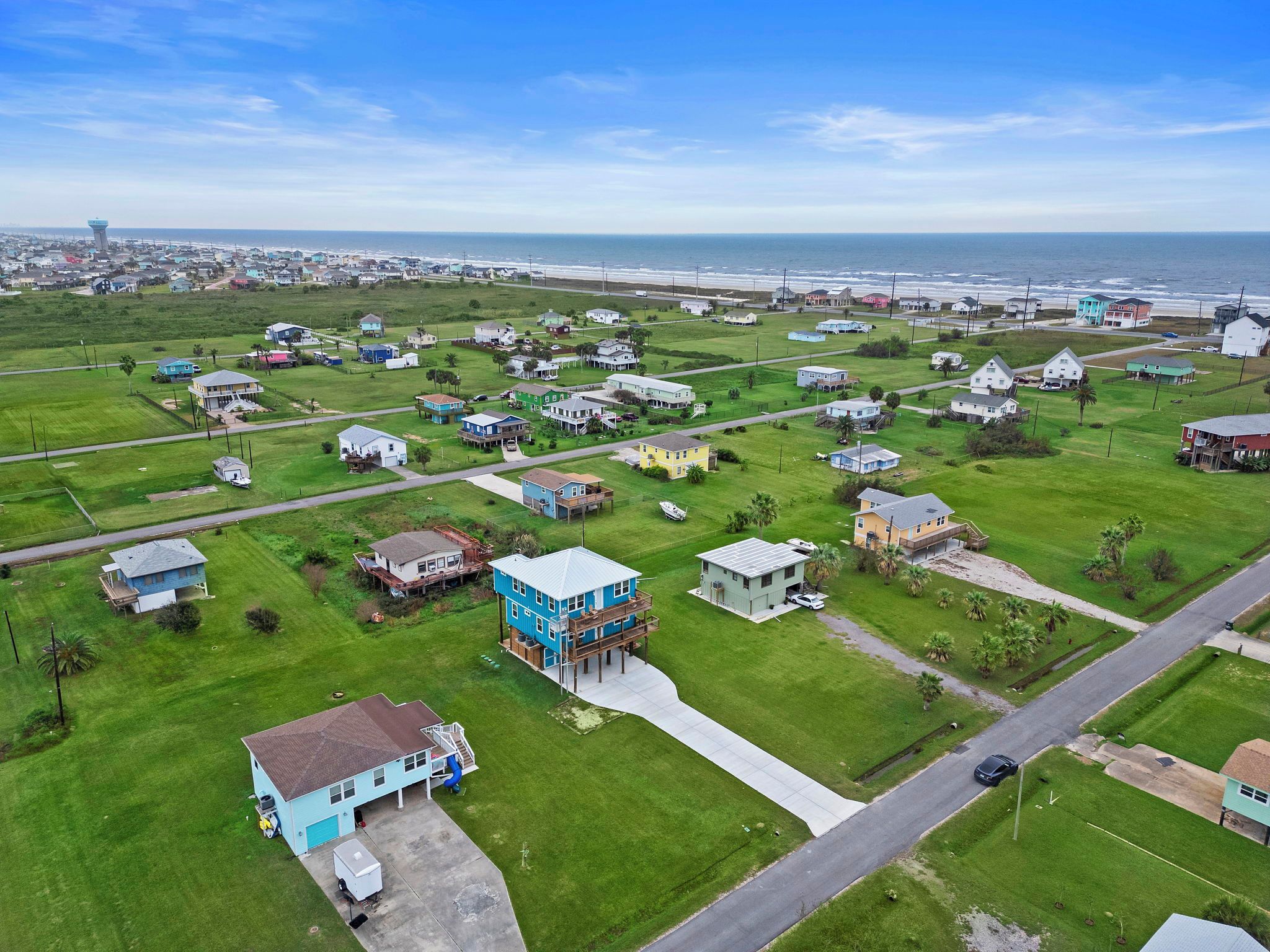 An aerial view of a coastal residential area with houses, roads, and a lighthouse in the distance.