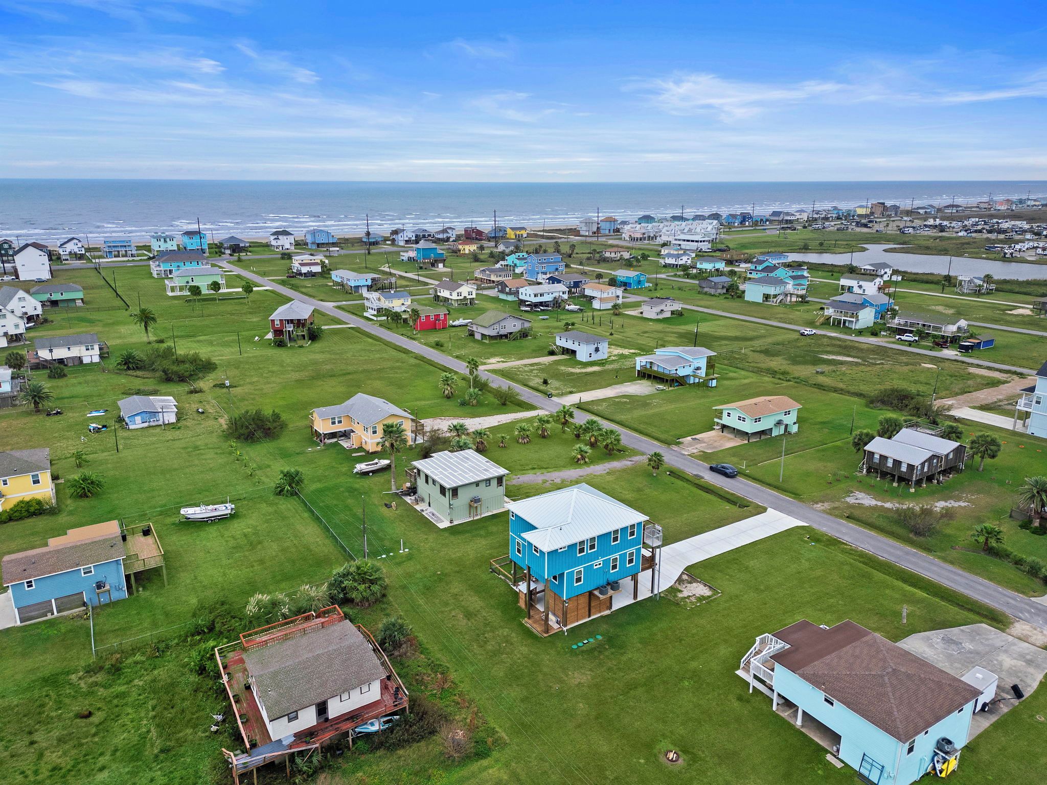 An aerial view of a coastal residential area with houses, roads, and a beach in the background.