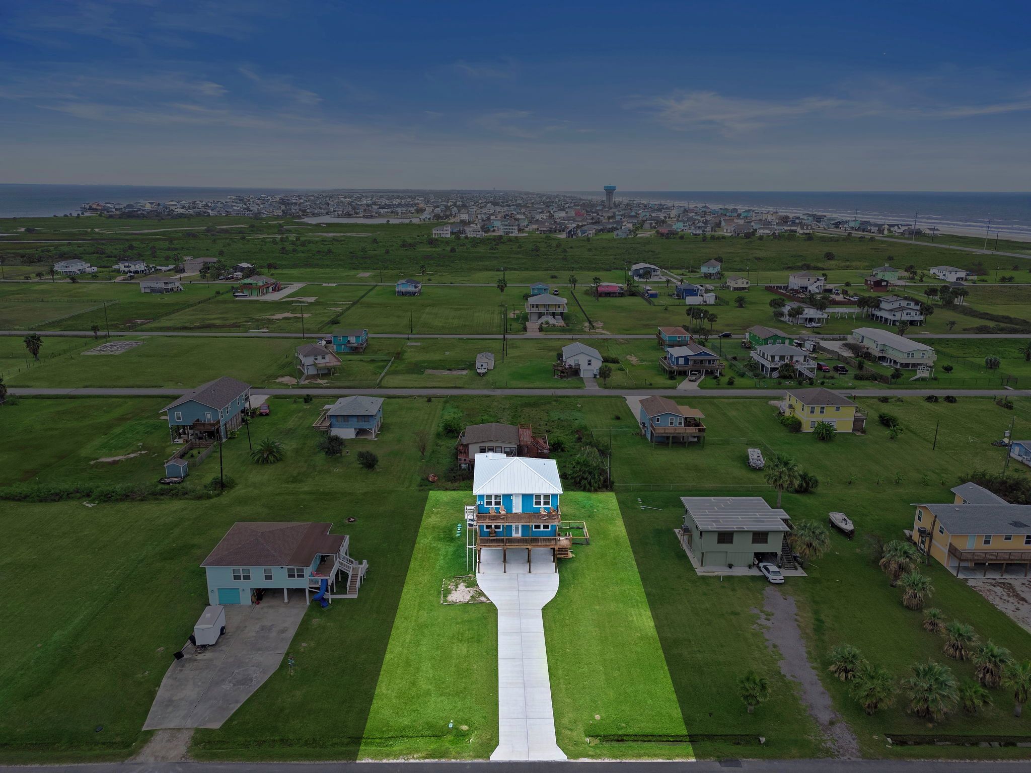 An aerial view of a residential area with houses, green lawns, and a clear sky.