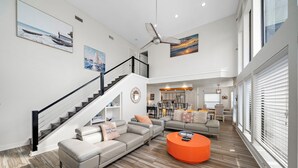 A spacious living room with a staircase, a ceiling fan, and a dining area. - Ocean View by Ryson Vacation Rentals (Galveston)
