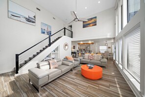 A spacious living room with a staircase, a ceiling fan, and a dining area. - Ocean View by Ryson Vacation Rentals (Galveston)