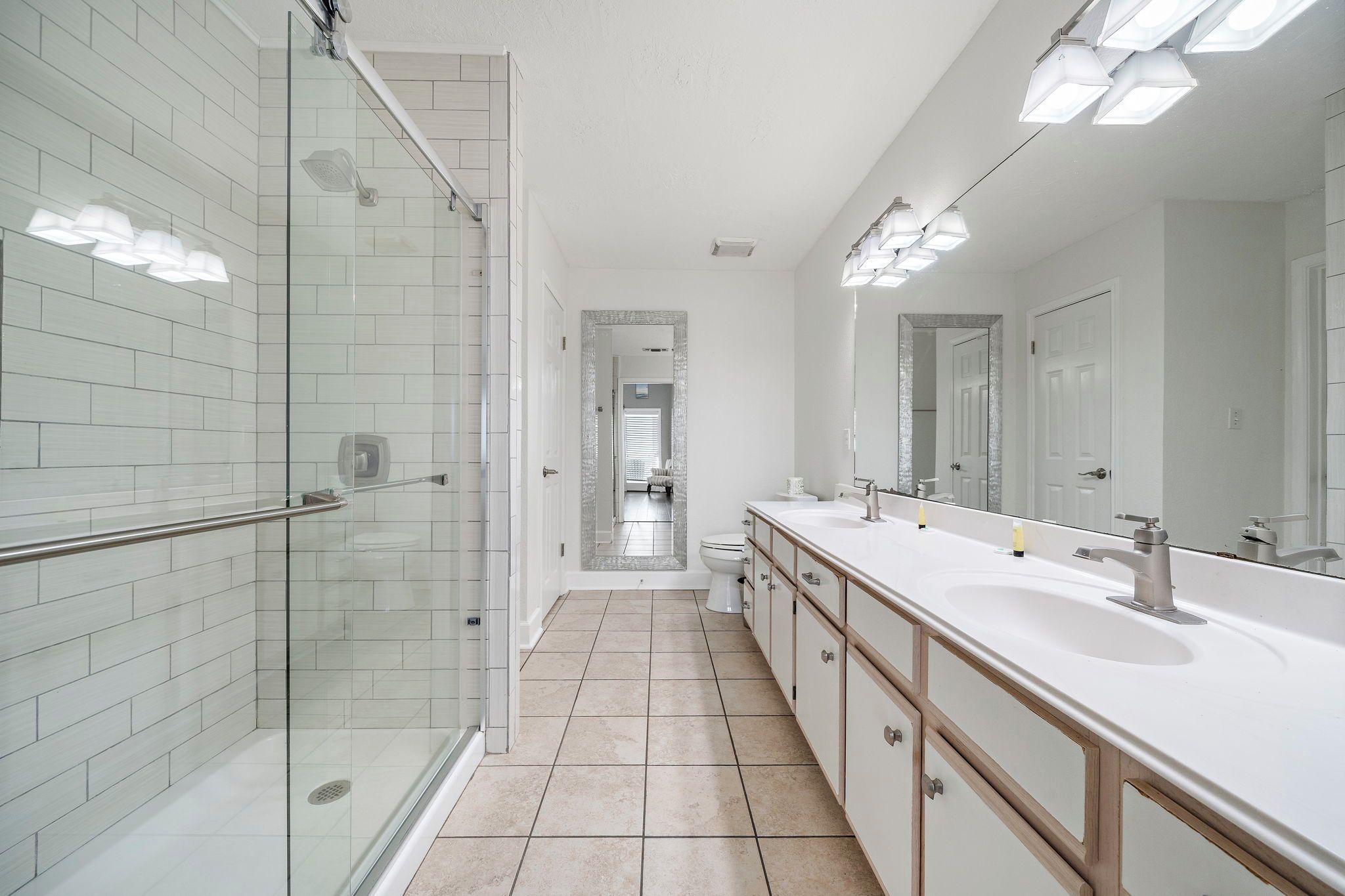 A modern bathroom with a glass shower enclosure, a large mirror, and a double sink vanity.