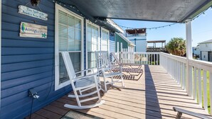 A wooden deck with rocking chairs, a covered porch, and a white picket fence. - Island Breeze by Ryson Vacation Rentals (Galveston)