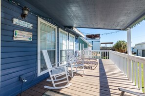 Una terraza de madera con mecedoras, un porche cubierto y una valla de piquetes blanca.