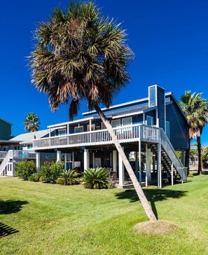 A two-story building with a balcony, a staircase, and a palm tree in the foreground. - Island Breeze by Ryson Vacation Rentals (Galveston)
