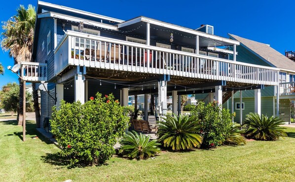 A two-story house with a balcony, surrounded by well-maintained lawns and tropical plants.