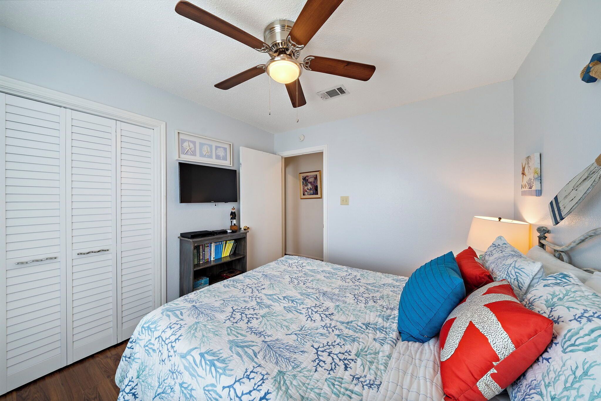 Une chambre à coucher comprenant un lit, un ventilateur de plafond, une armoire, un téléviseur et une bibliothèque.
