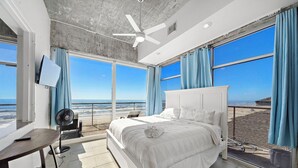 Une chambre avec un grand lit, un ventilateur de plafond, une télévision et une vue sur la plage.