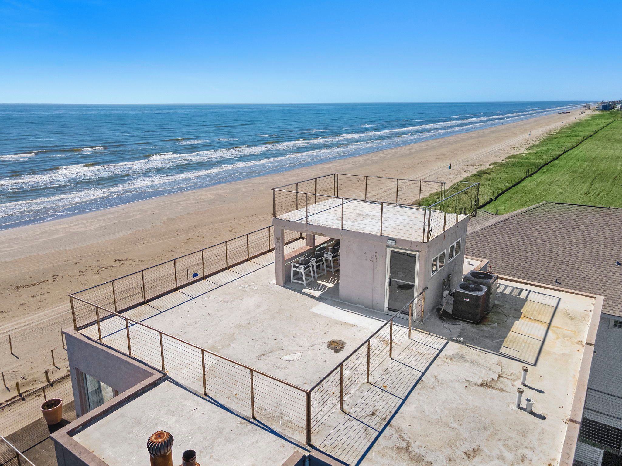 Ein Gebäude direkt am Strand mit einer umzäunten Terrasse, einem kleinen Pool und einem Rettungsturm.