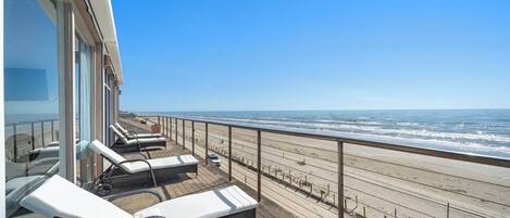 A deck with sun loungers overlooking a beach.