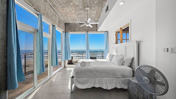 A bedroom with a large bed, a ceiling fan, and a view of the beach.