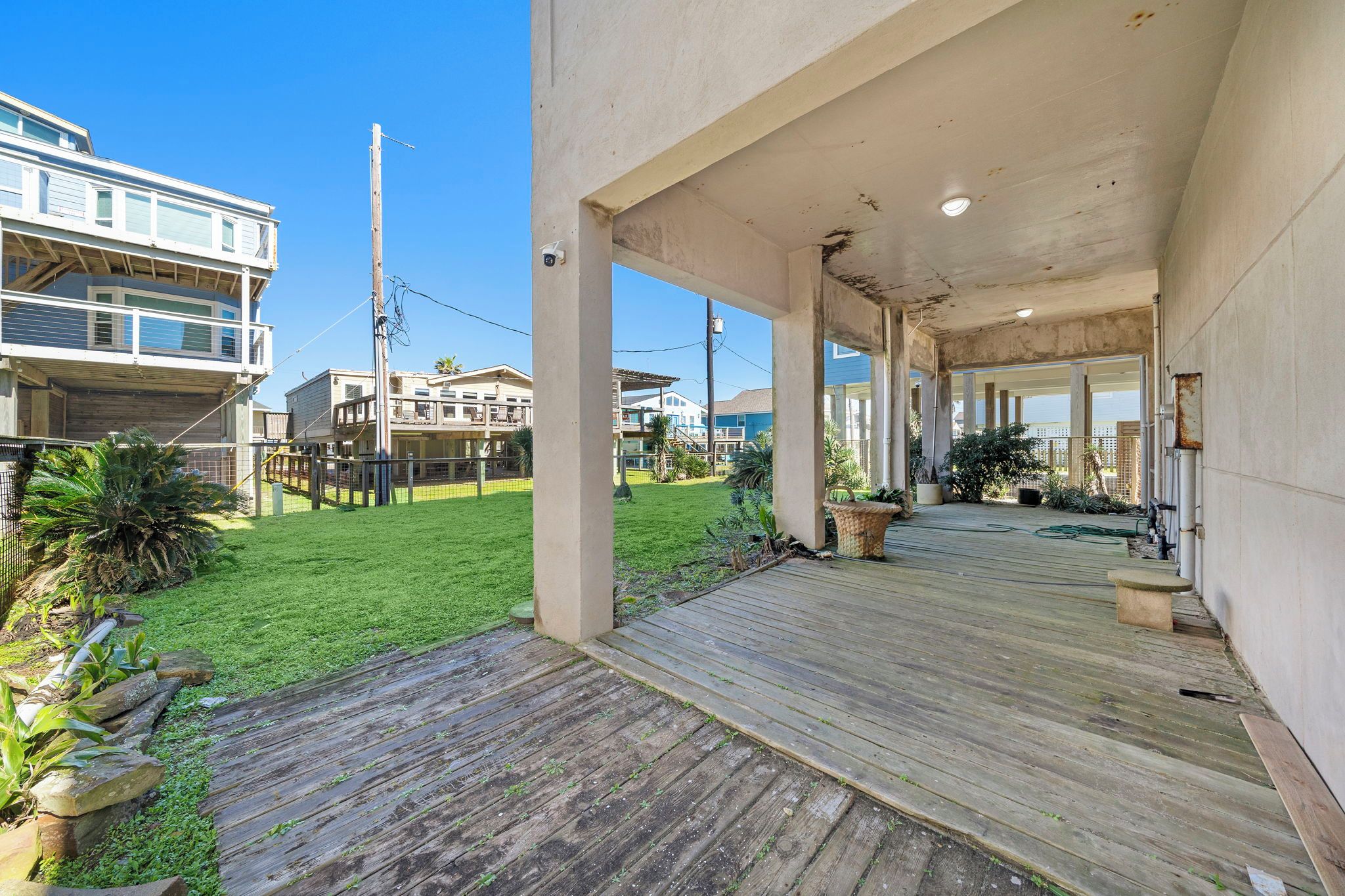 A covered outdoor area with a wooden deck, a grassy lawn, and a view of neighboring buildings.