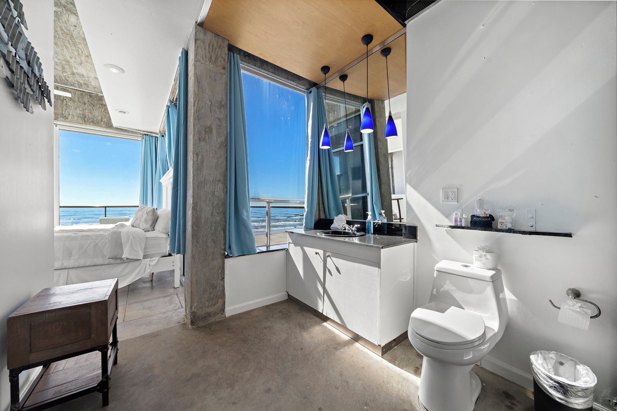 Un baño moderno con inodoro, lavabo y ventanas amplias con vistas al mar.
