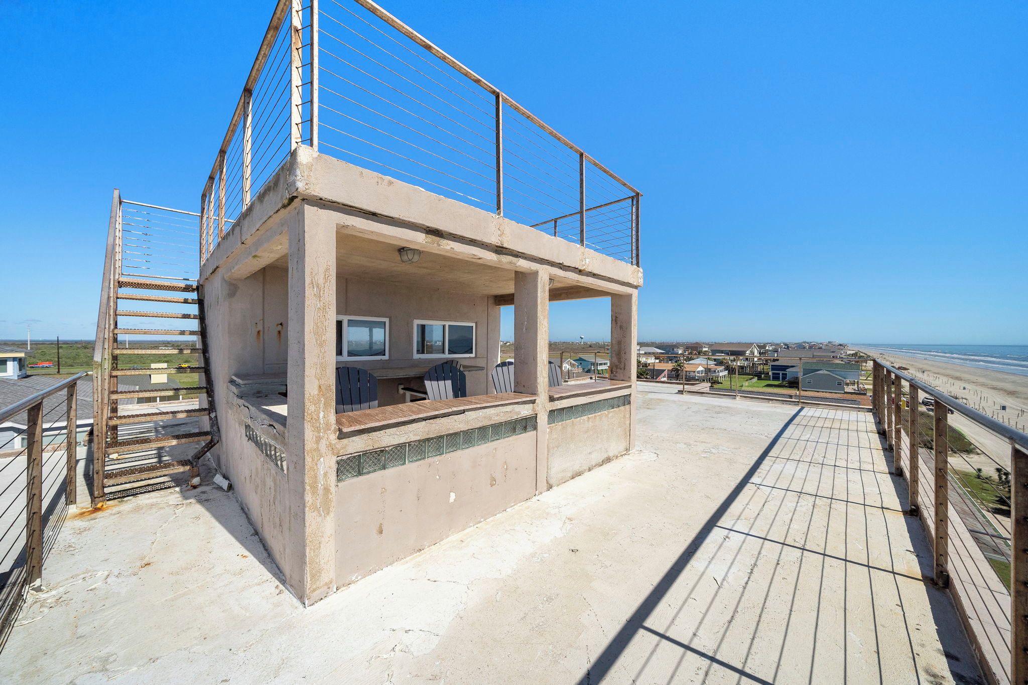 A beachside lifeguard tower with a wooden deck and metal railing, overlooking the ocean.