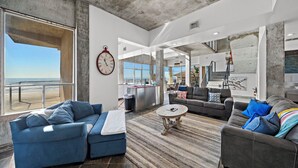 Un vaste espace de vie avec une grande fenêtre donnant sur l’océan, une cuisine moderne et un coin salon confortable avec des canapés et une table basse.