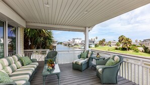 A covered outdoor deck with a sofa, chairs, and a small table. - Luna Mar by Ryson Vacation Rentals (Galveston)