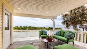 A covered patio with green cushioned seating, a table with a potted plant, and a view of the ocean. - Luna Mar by Ryson Vacation Rentals (Galveston)