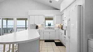 A modern kitchen with white cabinets, a large island, and a view of the ocean. - The Beach House by Ryson Vacation Rentals (Galveston)