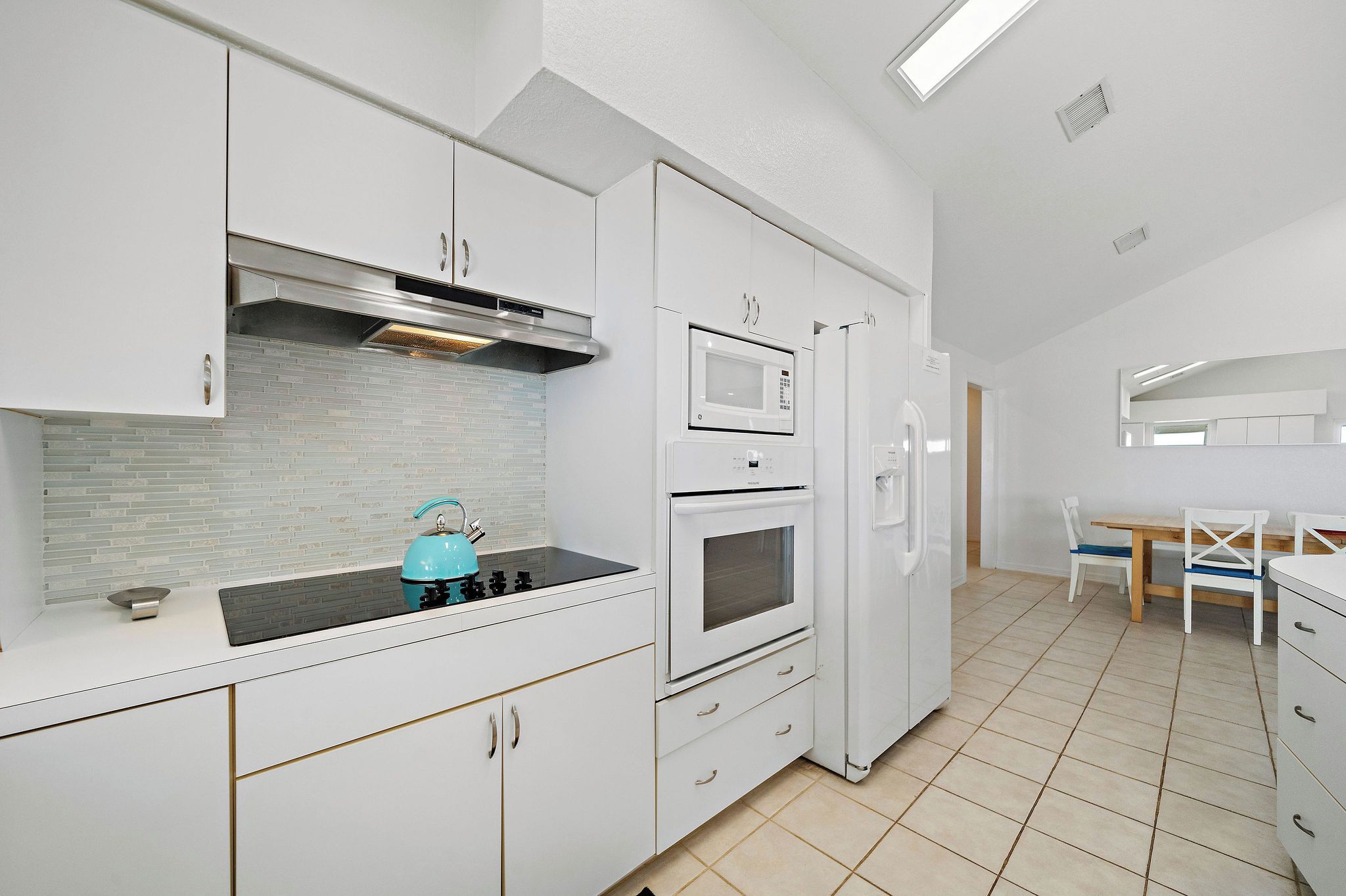 A modern kitchen with white cabinets, a microwave, oven, and a kettle on the counter.