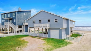 A two-story beachfront house with a covered porch, a garage, and a white picket fence. - The Beach House by Ryson Vacation Rentals (Galveston)