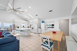 A spacious living area with a large sofa, a wooden dining table, and a kitchen in the background.