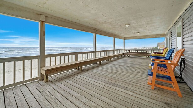 A wooden deck with a bench and colorful chairs, overlooking the ocean. - The Beach House by Ryson Vacation Rentals (Galveston)