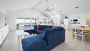 A spacious living area with a large blue sectional sofa, a dining table with chairs, and a kitchen in the background. - The Beach House by Ryson Vacation Rentals (Galveston)