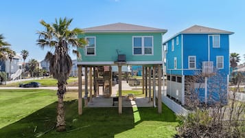 A two-story house with a covered porch and a small deck, surrounded by a well-maintained lawn and palm trees.