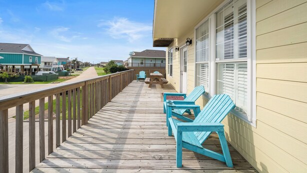 A wooden deck with blue chairs and a picnic table, overlooking a residential street. - The Krusty Krab by Ryson Vacation Rentals (Galveston)