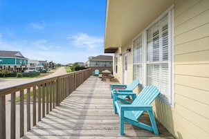 A wooden deck with blue chairs and a picnic table, overlooking a residential street.