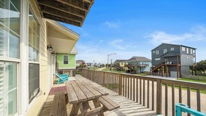 A wooden deck with a picnic table and chairs, overlooking a residential street with houses and a clear sky. - The Krusty Krab by Ryson Vacation Rentals (Galveston)
