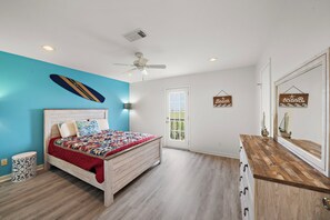 A bedroom with a bed, a ceiling fan, and a door leading to a balcony.