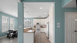 A modern kitchen with white cabinets, a microwave, and a dining area with a table and chairs. - The Krusty Krab by Ryson Vacation Rentals (Galveston)