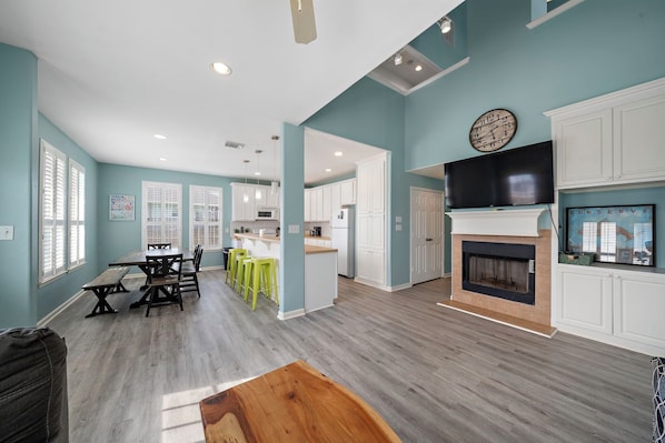 A spacious living area with a dining table, kitchen, and fireplace. - The Krusty Krab by Ryson Vacation Rentals (Galveston)