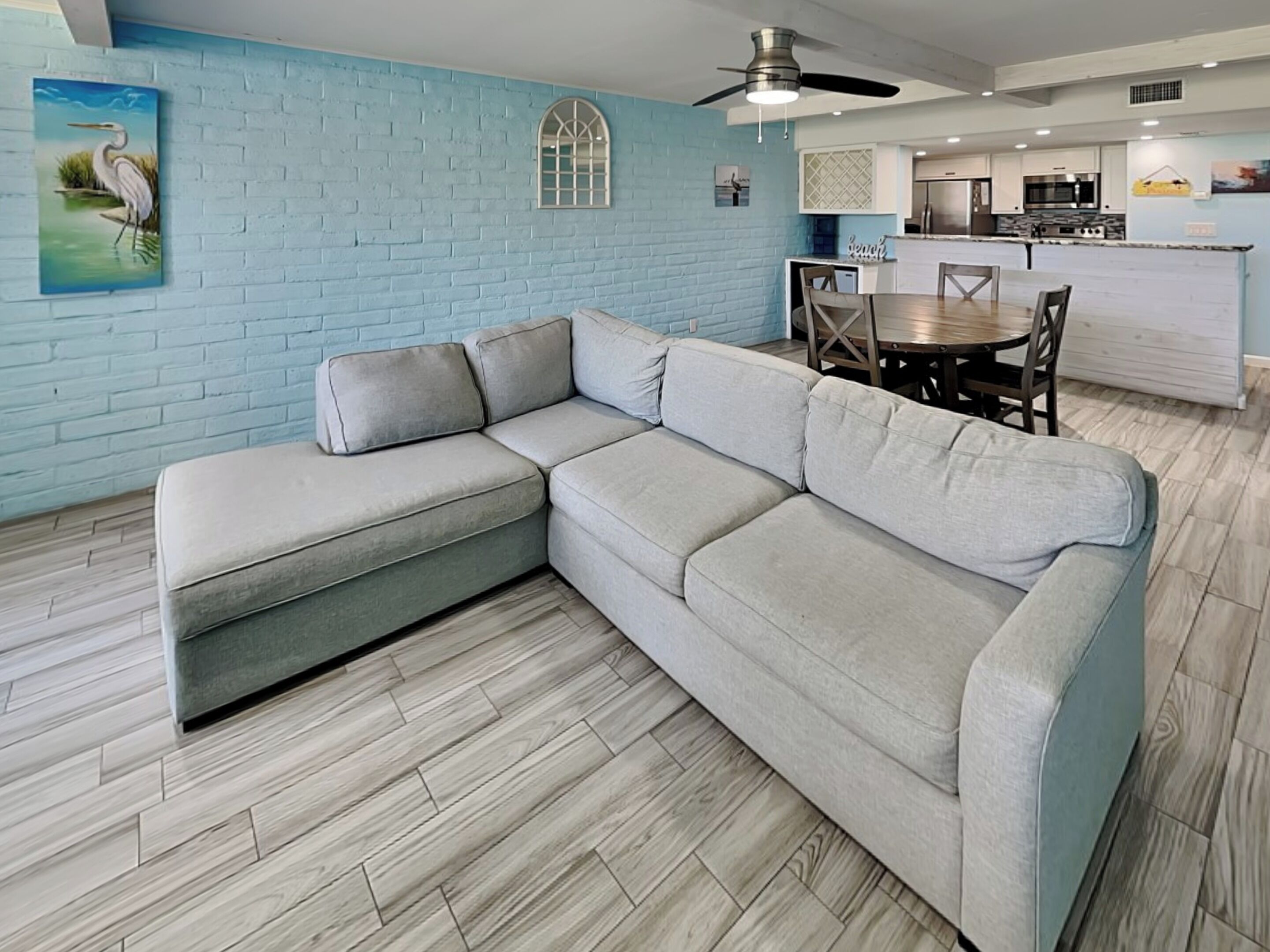 Ein modernes Wohnzimmer mit Ecksofa, Esstisch mit Stühlen, Küchenzeile und Deckenventilator.