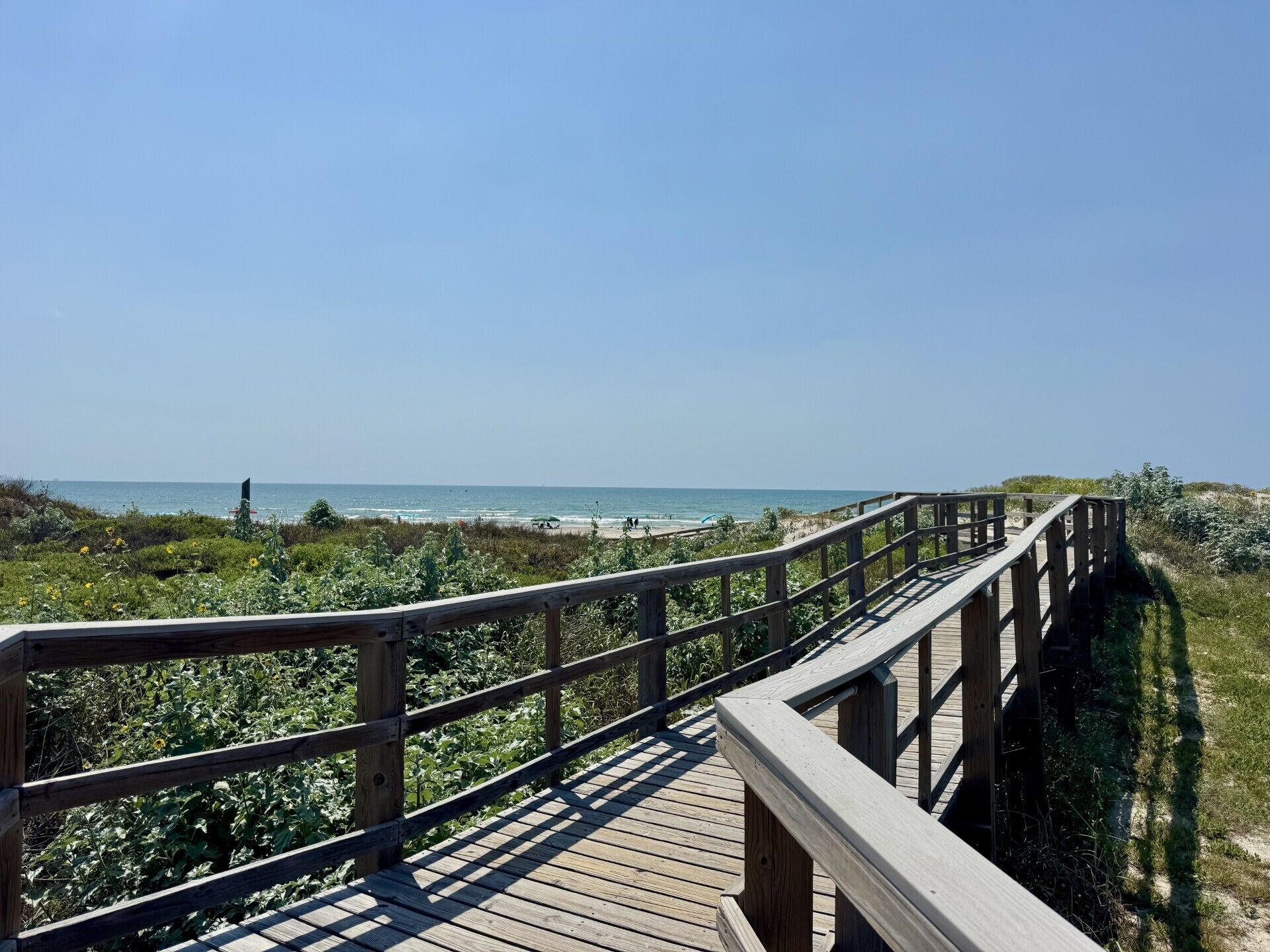 A wooden boardwalk leading to a beach with clear skies.