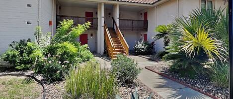 A two-story building with a covered outdoor area, a staircase, and a variety of plants.