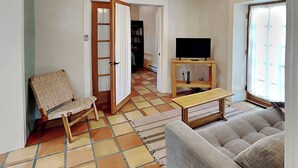 Ein Wohnzimmer mit einer Couch, einem Holztisch, einem Korbstuhl, einem Fernseher auf einem Holzboden und einem Fliesenboden.