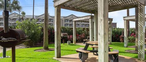 A wooden gazebo with a pergola roof, surrounded by a well-maintained lawn and palm trees.