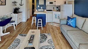 Un espacio habitable compacto con kitchenette, zona de comedor con mesa y sillas, sofá y ventilador de techo.