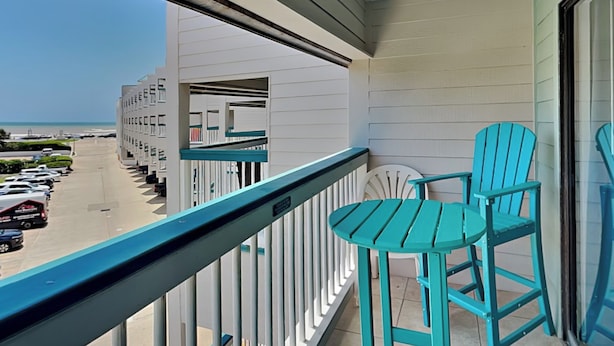 A balcony with turquoise chairs and a view of a parking lot and buildings.